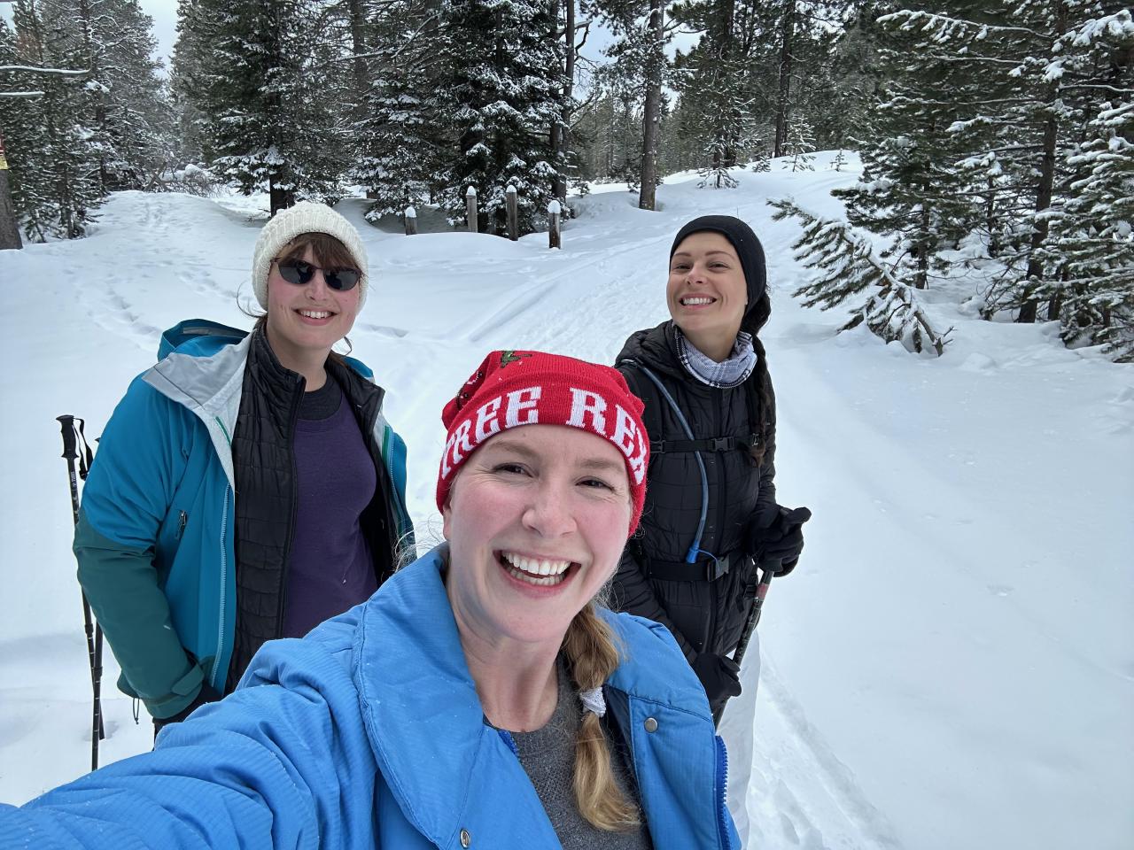 A selfie of three people: me and two friends, wearing cold weather gear and standing in the snow. A well-traveled path in the snow meanders through the snow-covered trees.