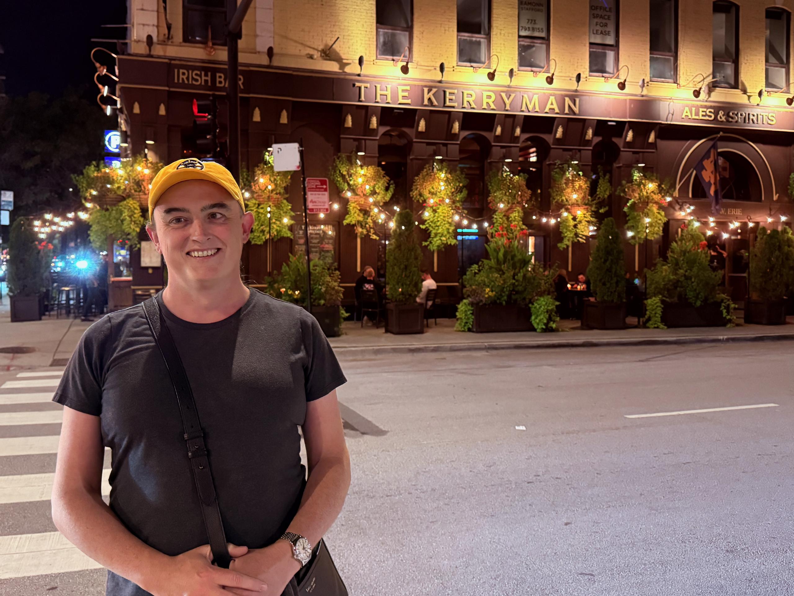 The Kerryman is a great Irish bar in River North, owned and operated by one of Tess' distant Irish cousins.
Tess, on the left, stands outside a large pub on a stree corner. The pub has outdoor seating.