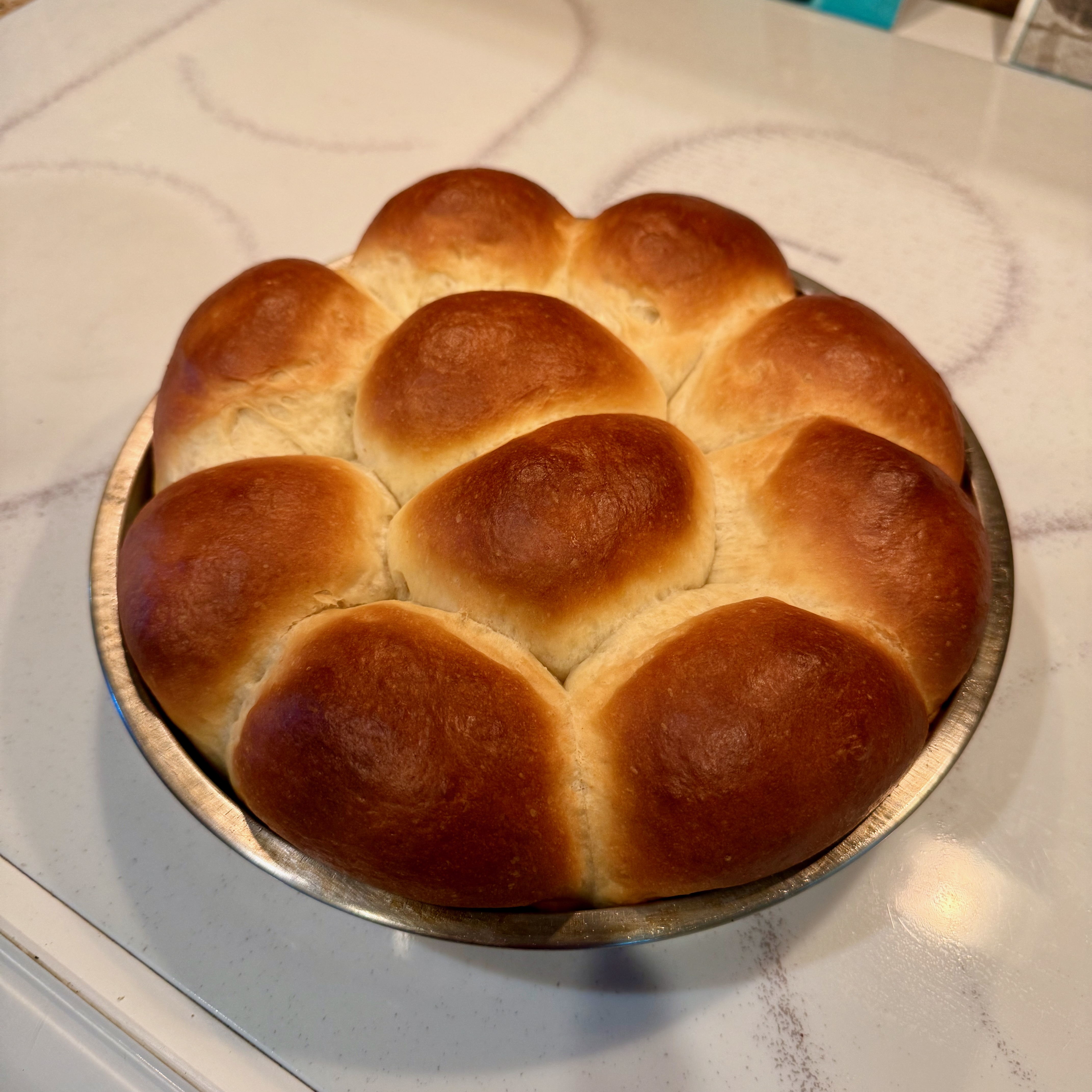 A set of ten rolls with golden brown tops arranged in a circular cake pan.
